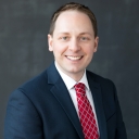 Headshot of Dustin Evatt-Young: man in a blue suit with a white shirt and red tie, smiling