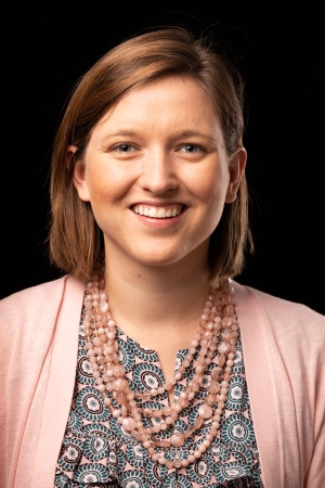 Headshot of Ashley Pennell - woman wearing pink sweater, patterned shirt and pink necklace