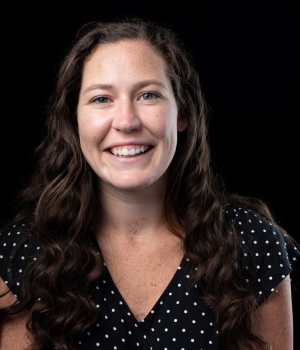 Headshot of Carly May with long, brown hair and a polka dot shirt